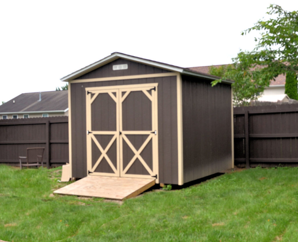 painted wood utility shed with brown siding, tan trim, and wood ramp