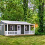 she shed with green siding, front porch white white vinyl railings, and metal roof