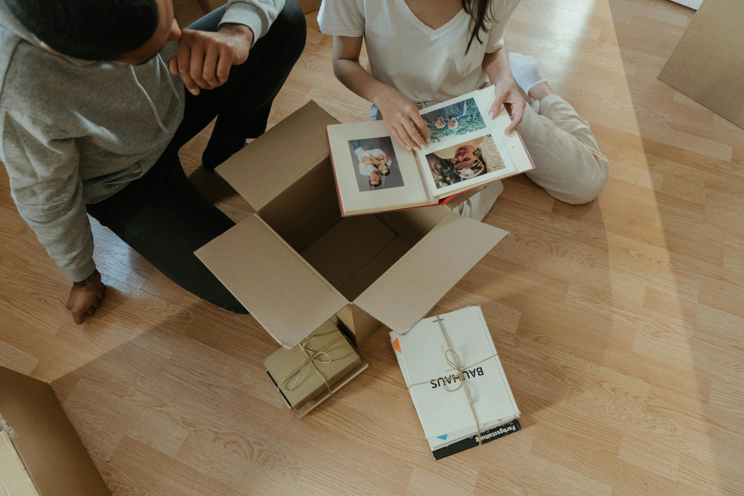 Overhead shot of two people sitting on the floor next to a cardboard box and looking at a photo album