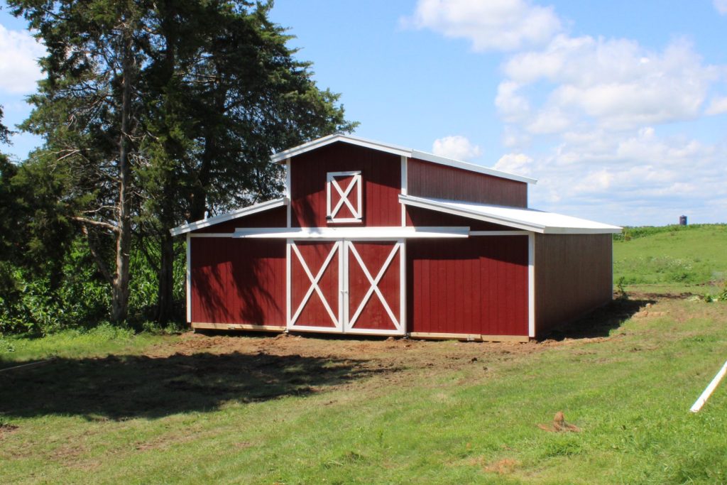 Front exterior of a monitor horse barn with red siding, white trim, sliding barn doors, and white roofing.