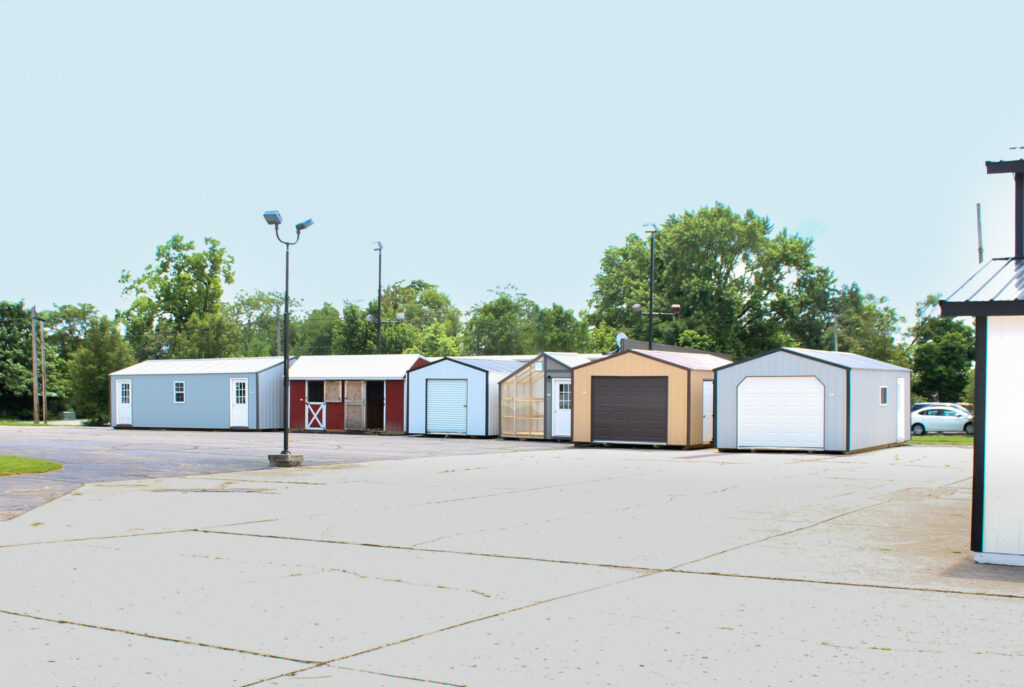 An assortment of storage buildings in a line on a lot including garages, a greenhouse, a horse barn, and sheds.