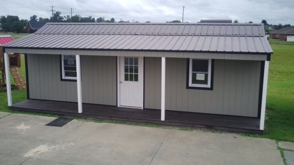Raber Seymour office with gray wood siding, black trim, a gray metal roof with an overhang, white posts, a dark front porch, 2 white windows, and a white front door with windows.