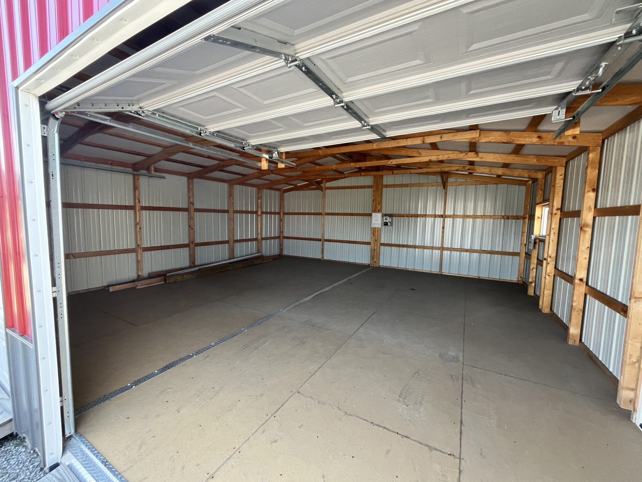 Interior of a 24x24 two-car garage with metal siding, a small window, and flooring.