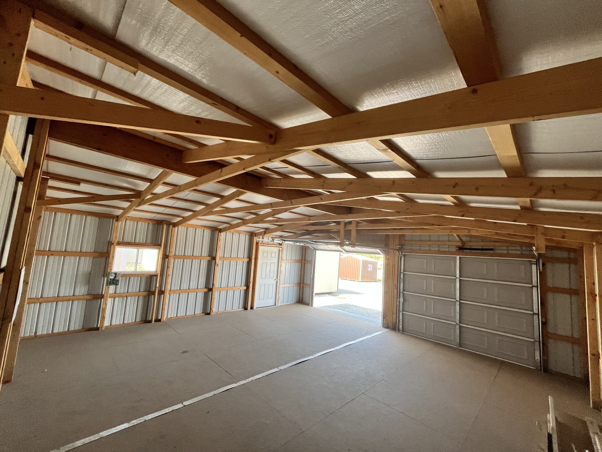 Interior of a 24x24 two-car garage with metal siding, a small window, 2 garage doors, and flooring.